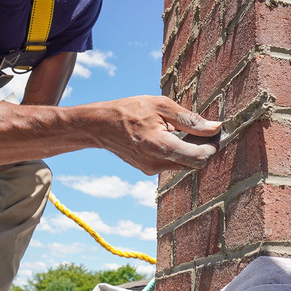 Tuckpointing mortar joints on a brick chimney